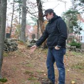 Life-long resident Steven Jollimore points to a location just beyond the cemetery walls where fragments of a casket dating back to the 1850's were found after the road construction.  Photo Robert Devet