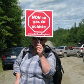 A woman uses her shale gas protest sign as shade during a hot afternoon at the seismic truck blockade in Stanley. Photo: Tracy Glynn. 